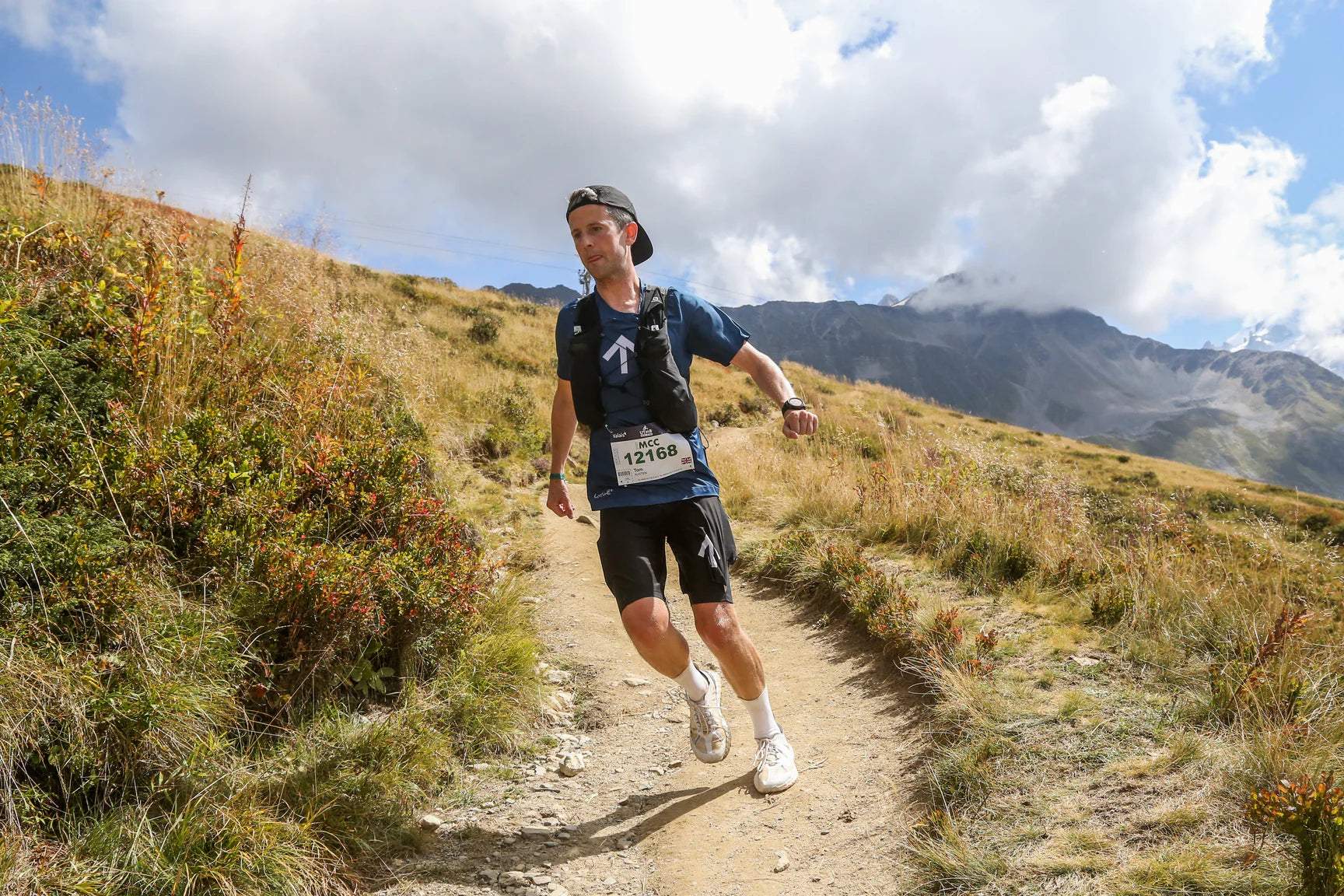Man running on a mountain trail with mountains and blue sky in the background