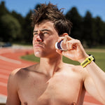 An athlete is applying the Pelotan 2oz roll-on to their face while stood beside a running track.