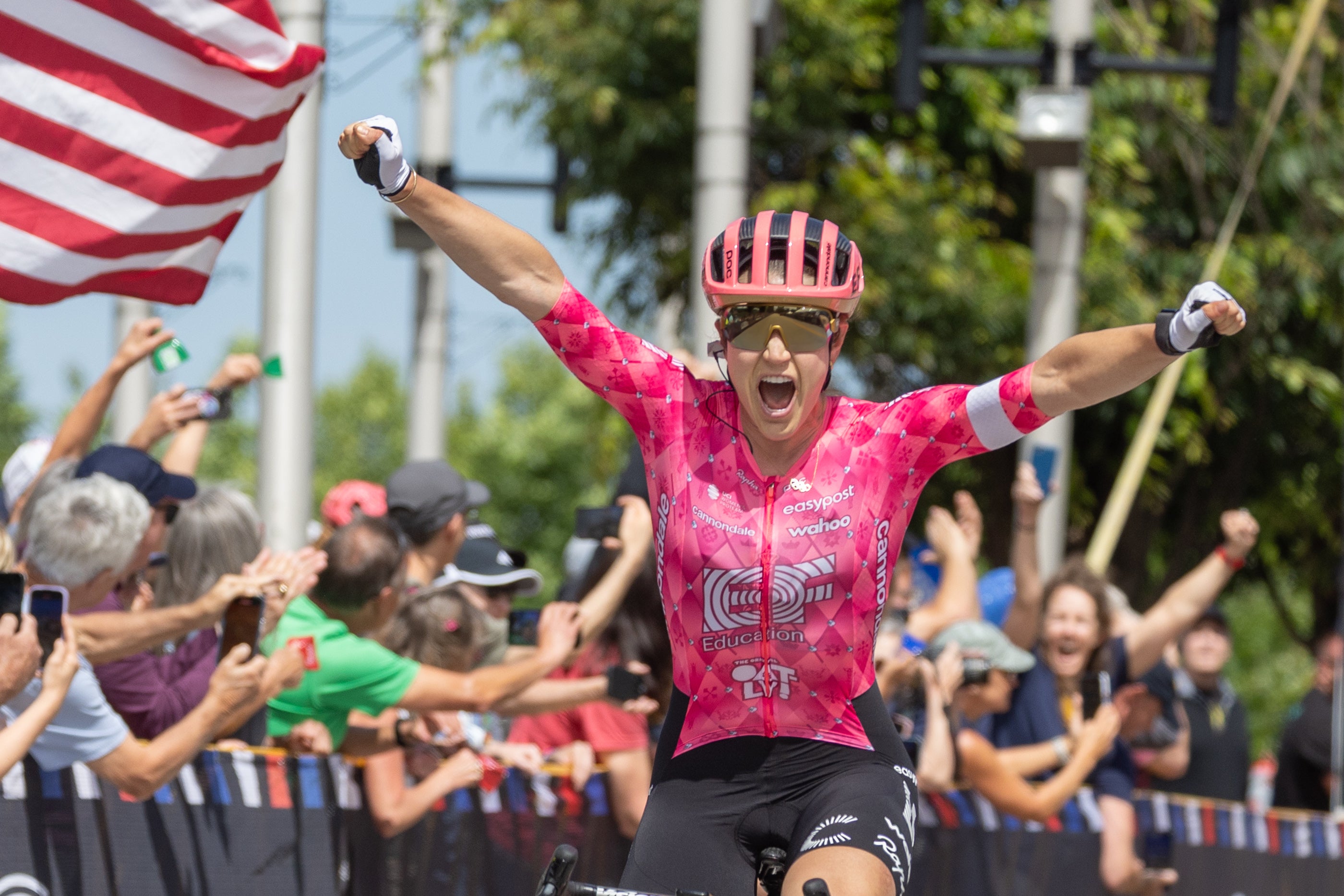 Cyclist in a pink jersey celebrating with arms outstretched in front of a crowd.