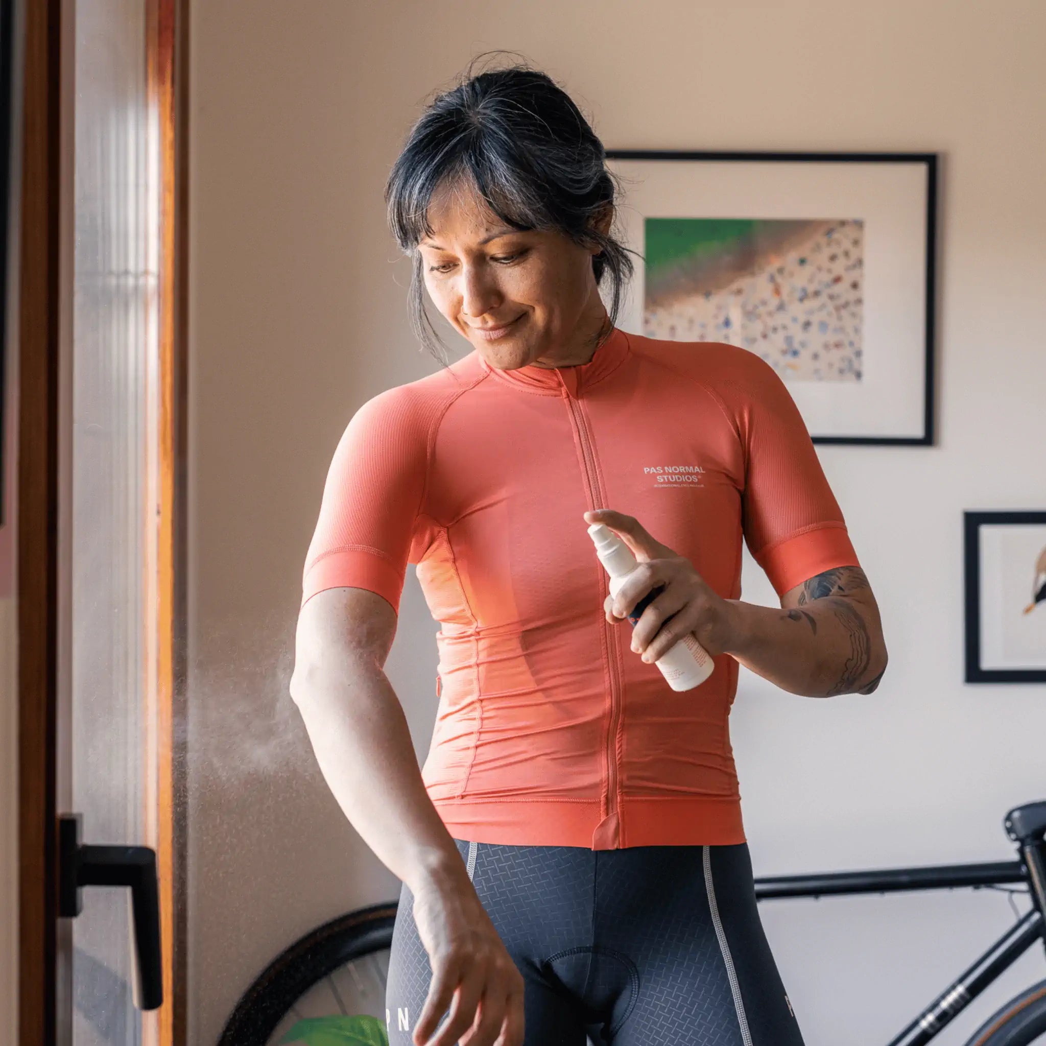 A female cyclist is applying a spray of Pelotan performance sunscreen at home, before leaving for a ride.