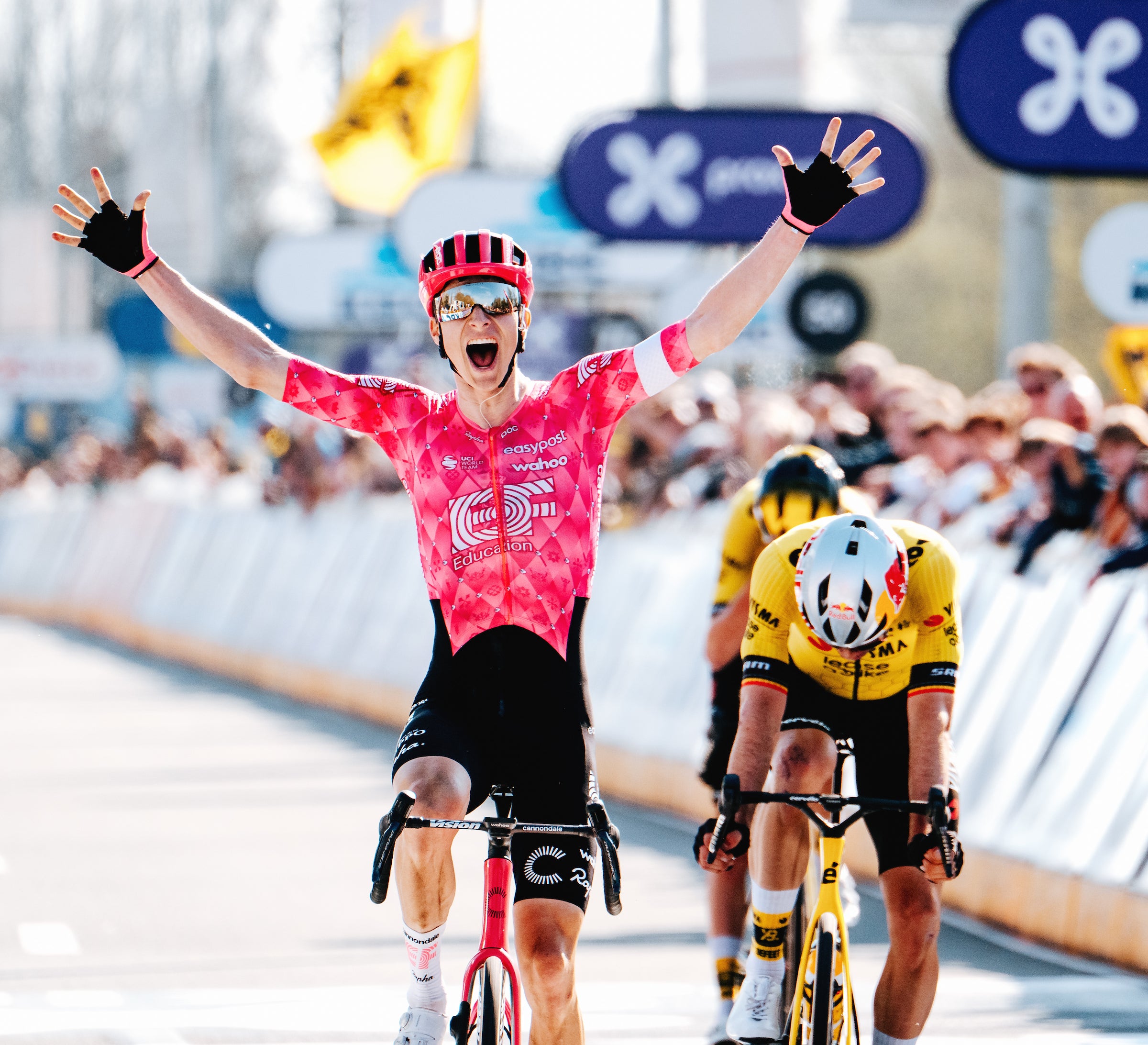 Cyclist in a pink jersey celebrating a victory on a bicycle with other cyclists in the background.