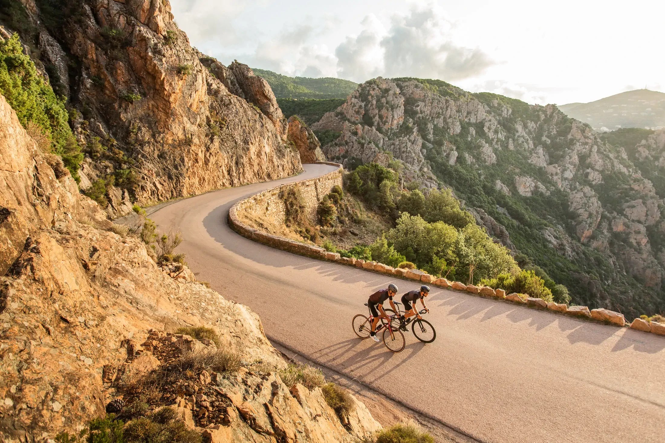 Two cyclists on a winding mountain road with scenic views of Corsica.
