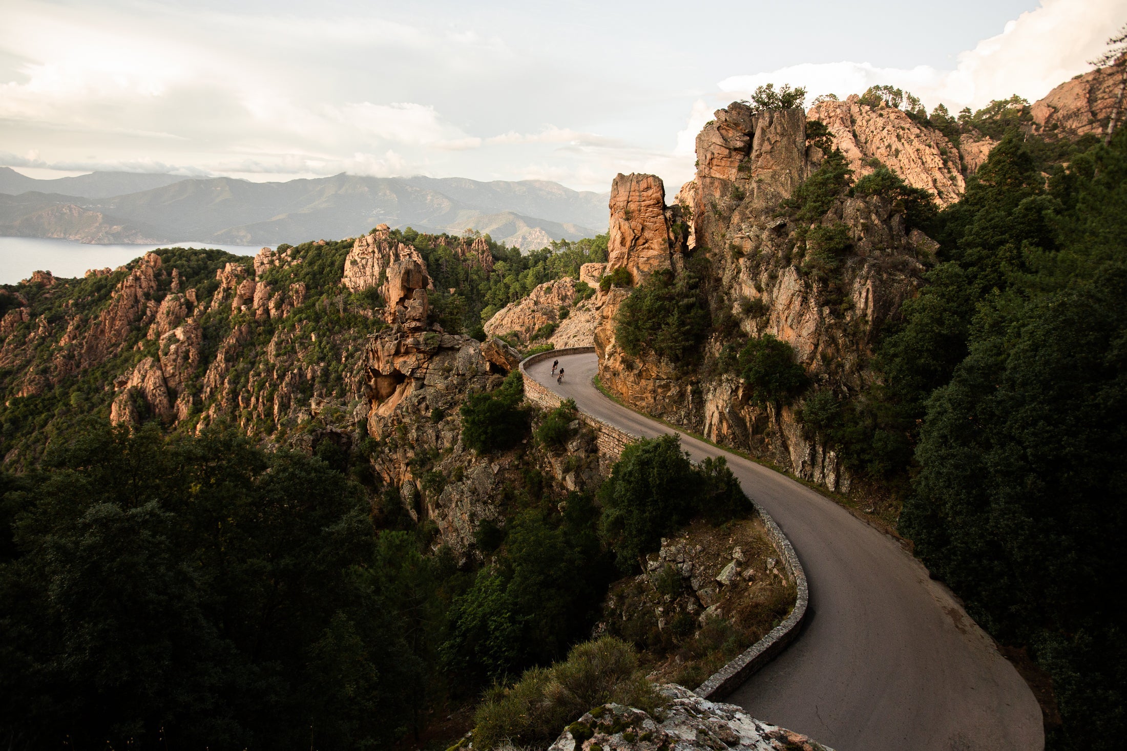 A winding Corsican road through a mountainous landscape with rocky cliffs and greenery.