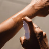 An image showing a female athlete applying the spray bottle of Pelotan Performance Sunscreen on a sunny day.