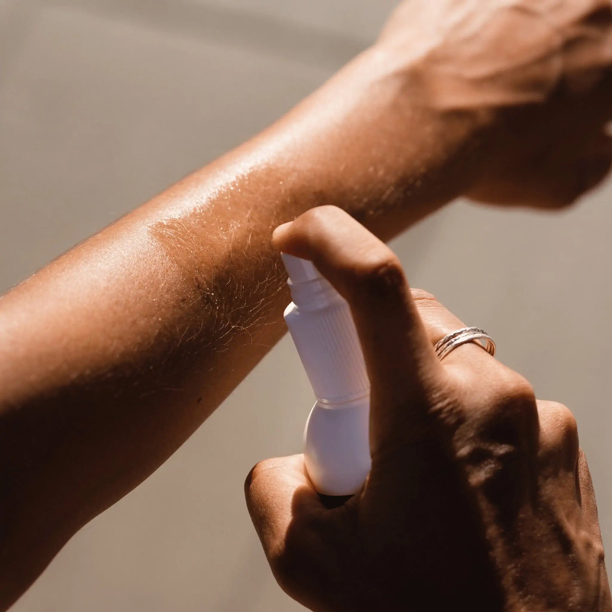 An image showing a female athlete applying the spray bottle of Pelotan Performance Sunscreen on a sunny day.