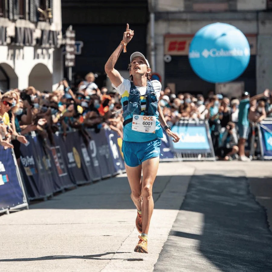 Athlete crossing the finish line in a marathon with a crowd and balloons in the background.