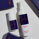 Two bottles of Peloton sunscreen on a light surface with boxes in the background.