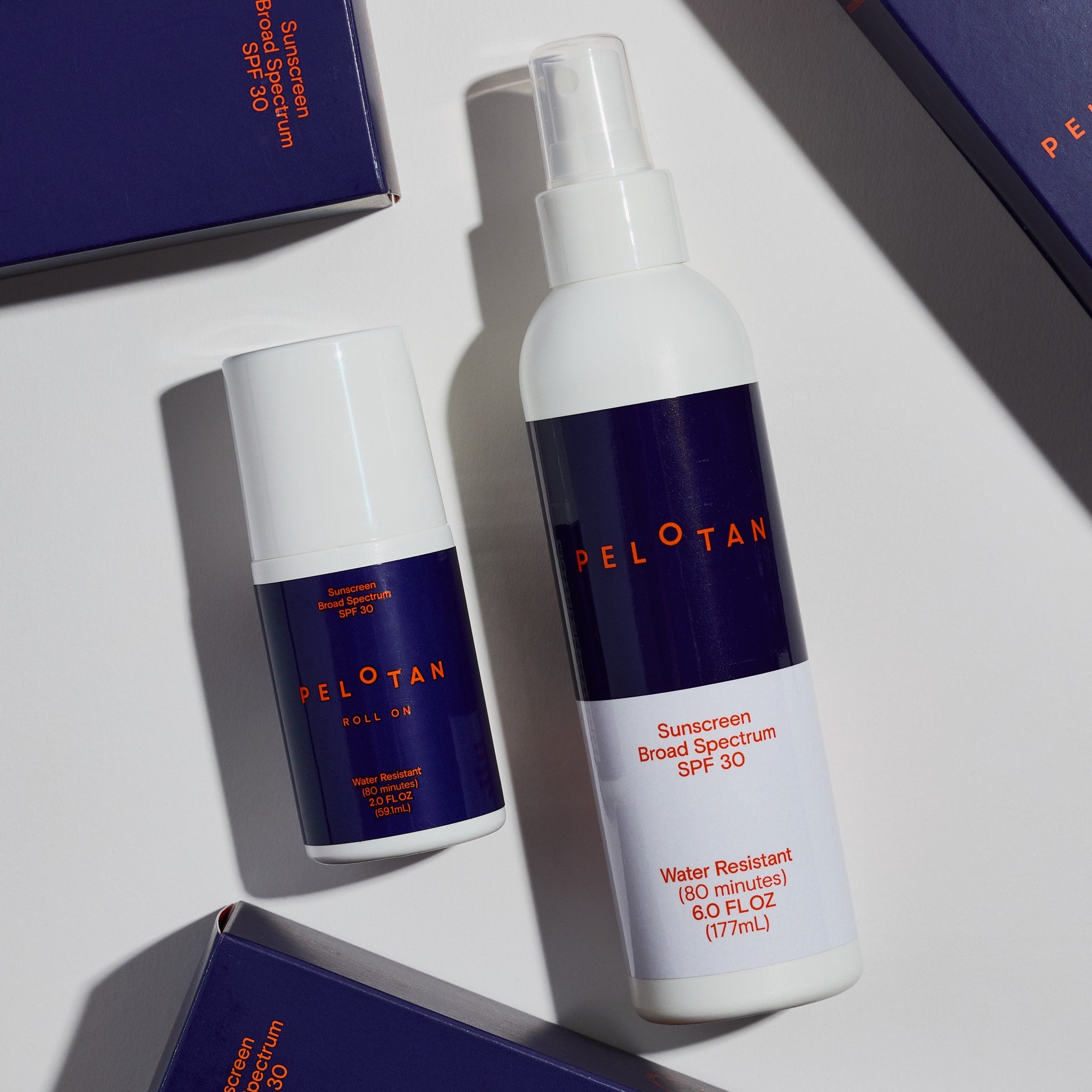 Two bottles of Peloton sunscreen on a light surface with boxes in the background.