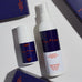 Two bottles of Peloton sunscreen on a light surface with boxes in the background.